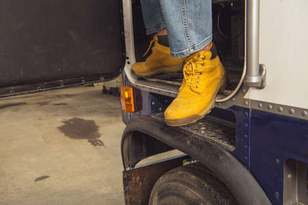 Closeup of Trucker's Legs in Orange Boots Stepping Out of the Truck After Successfully Completing a Route. The End of the Job. Transportation Theme.の写真素材