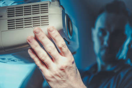 Home Theater in the Making. Closeup at the Multimedia Projector Being Adjusted by Caucasian Men to Regulate the Projected on a Wall Image.の写真素材