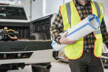 Closeup of Caucasian Supervisor Wearing Yellow Warning Safety Waistcoat with Blueprint Building Plan...
