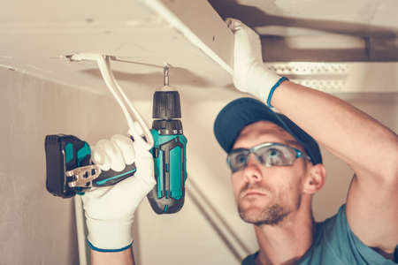 Closeup of Caucasian Contractor in His 40s Focused on Installation of the Gypsum Plasterboard Using Electric Screwdriver. Construction Site Industrial Theme.の写真素材