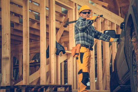 Caucasian Contractor Holding a Hammer on His Shoulder While Opening His Pickup Truck to Pack Up His...