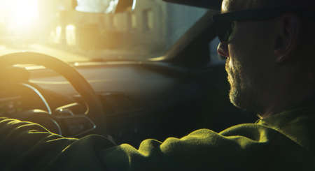 Caucasian Men Wearing Black Sunglasses Driving His Modern Sporty Car During Scenic Sunset. Automotive Industry Concept Photo.の写真素材