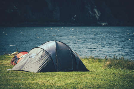 Closeup of a Tent Pitched on the Green Lake Shore with Mountain Wall in the Background. Scenic Camping Spot. Traveler Lifestyle. Outdoor Stay Theme.の写真素材
