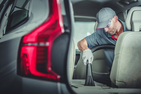 Caucasian Auto Detailer Precisely Vacuuming Folded Down Car Back Seat During Premium Vehicle Interior Cleaning Service.の写真素材