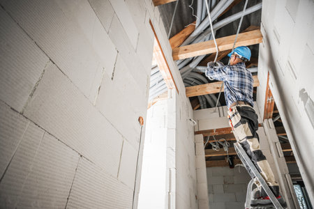 Professional Electrician Installing Electric Line Along Ceiling in Newly Concrete Built Building.