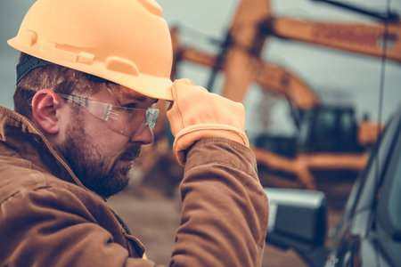 Closeup of Professional Construction Worker Wearing Yellow Hard Hat, Protective Glasses and Gloves. Industrial Safety Equipment Theme.の写真素材