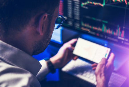 Caucasian Professional Trader in Front of Smartphone and Desktop Computer Display Focused on a Price...