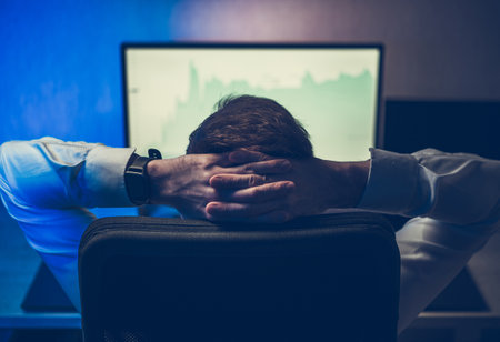 Satisfied Trader Sitting Relaxed in His Office Chair in Front of Computer Monitor Looking at Stock Market Graphs. Successful Businessman.の写真素材