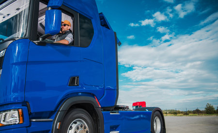 Caucasian Semi Truck Driver Awaiting a Trailer with Shipping Cargo. Truckers Theme. Lot parking.