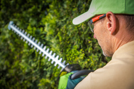 Side View Closeup of Professional Gardener Holding Hedge Trimmers Garden Power Tool. Blurred Background with Copy Space.の写真素材