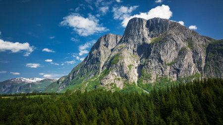 Colorful Summer Mountainscape in Vestland County, Norway, Europe. Large Rocky Mountain Surrounded by Green Forest. Blue Cloudy Sky in the Background.の写真素材