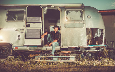 Caucasian American West Cowboy in His 40s Seating Relaxed in His Vintage Travel Trailer Doors. Trailer Restoration Projectの写真素材