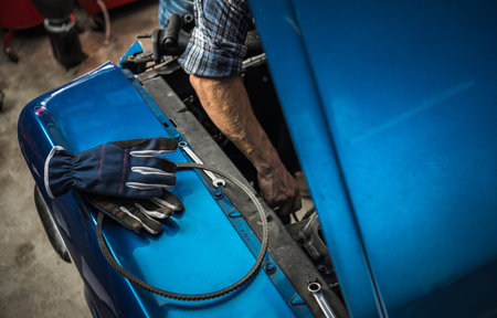 Caucasian Mechanic Taking Care of a Classic Car Engine. Performing Vehicle Maintenance.の写真素材