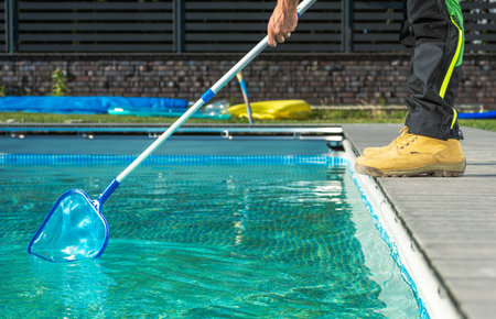 Caucasian Professional Pool Worker with a Pool Net Cleaning Residential Outdoor Swimming Poolの写真素材
