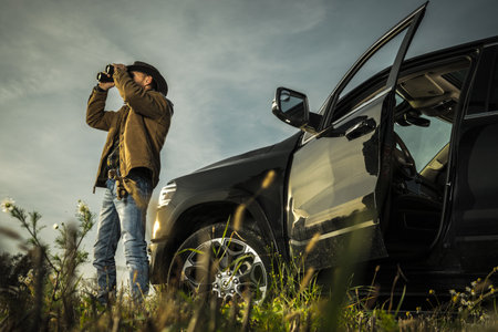 Caucasian Land Owner Staying Next to His Pickup Truck and Spotting Wildlife on His Ranch Using Binocularsの写真素材