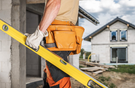 Caucasian Construction Worker with a Spirit Level in His Hand Walking Along the Site.の写真素材