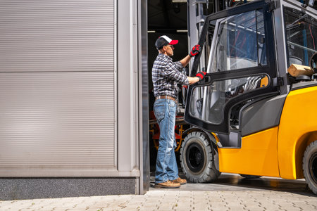 Caucasian forklift driver in his 40s maneuvering fork truck into warehouse.の写真素材