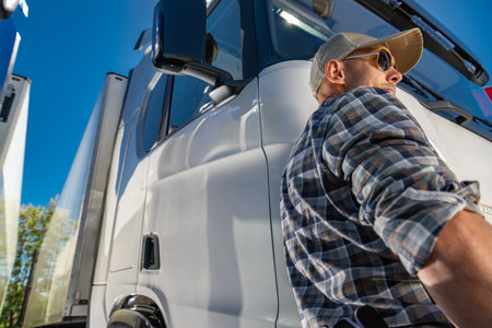 Proud caucasian professional semi truck driver in his 40s is standing in front of a truck.