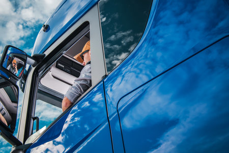 Truck driver is seated in the drivers seat of a blue truck. He is facing forward, ready to drive. The interior of the truck is visible, with the dashboard and steering wheel in focus.の写真素材