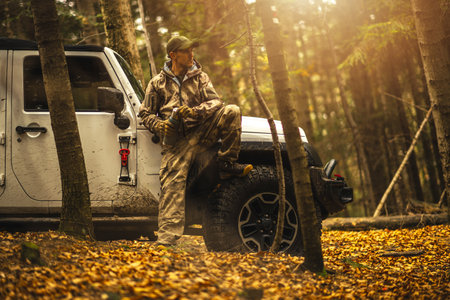 A man in camouflage clothing sitting on his SUV offroad vehicleの写真素材