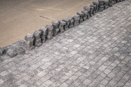 A neat arrangement of freshly laid cobblestones stretches across the foreground, while neatly stacked paving stones sit beside a sandy area. This scene captures the progress of urban development with precision and order.の写真素材