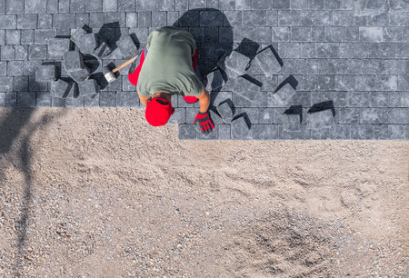 A worker carefully installs pavers in a residential backyard, breaking stones with a hammer on a sunny day.の写真素材