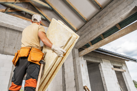 A construction worker carries insulation panels while preparing to install them in a residential...