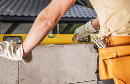A construction worker checks the level of a block wall using a leveling tool at a building site.の写真素材