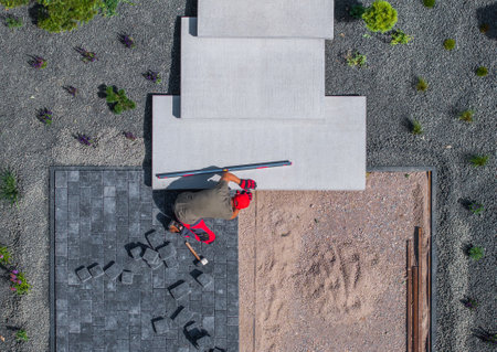 A man works on installing pavers in a well-designed outdoor space filled with gravel and grass.