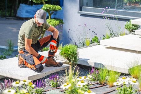 A gardener kneels on a path, planting flowers among decorative stones and greenery in a contemporary garden.の写真素材