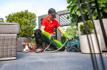 A gardener in gloves adjusts a hose reel as he prepares to water a variety of plants in a...