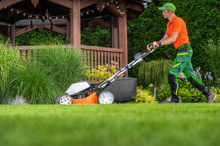 A diligent landscaper is mowing a vibrant lawn adjacent to a wooden gazebo, surrounded by ornamental...