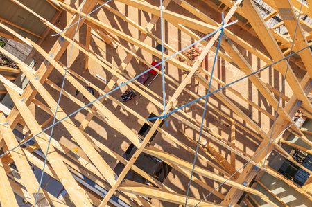 A construction site highlights a network of wooden beams and framework under bright sunlight,...