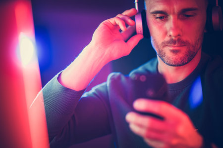 A man enjoys music using headphones while checking his smartphone in a dark setting, illuminated by colorful lights.の写真素材