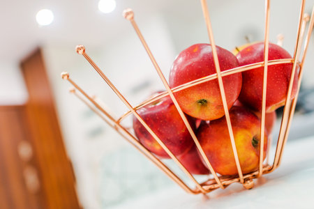 Bright red apples rest in a stylish copper wire bowl on a kitchen countertop, creating a vibrant and inviting atmosphere in a modern setting.の写真素材