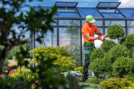 A gardener prunes green bushes in a vibrant botanical garden, showcasing lush plants and a...