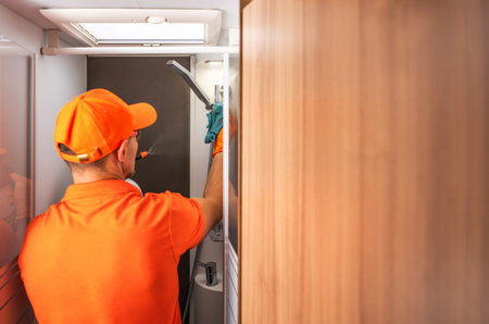 A maintenance worker in an orange uniform cleans RV camper van restroom fixturesの写真素材