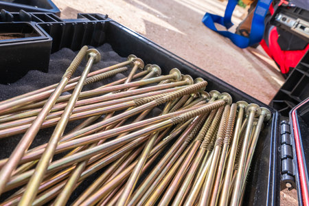 Long metal screws lie organized in a toolbox, highlighting the essential tools used during a construction project on a sunny day.の写真素材