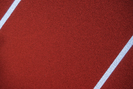 Red athletic track surface featuring white lane markings under a clear sky, inviting runners to...