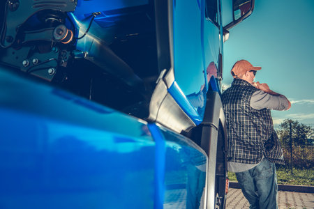 A truck driver stands beside his vehicle, enjoying a break outdoors on a sunny day. The scene captures the essence of long-haul trucking life.の写真素材