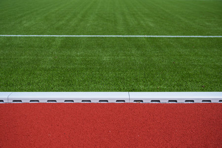 A well-maintained athletic field features vibrant green turf and a bright red running track. The scene captures the intersection of these two surfaces, inviting athletes to engage in sports and fitness activities.の写真素材
