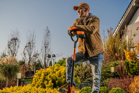 A gardener stands confidently with a shovel in hand, surveying a lush, colorful garden. The warm glow of the sunset highlights the vibrant plants around him, creating a serene and productive atmosphere as he plans his next steps.の写真素材
