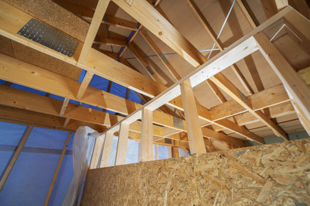 The interior of a house under renovation shows a wooden framework being constructed. The roof beams and supportive structures are prominently displayed, with protective coverings in place, indicating ongoing work.の写真素材