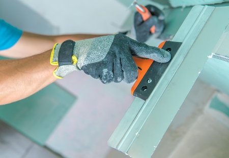 A person wearing protective gloves is applying a smoothing tool to a surface in a workshop. The focus is on the careful manipulation of the tool, ensuring a precise finish. The environment suggests an organized workspace.の写真素材