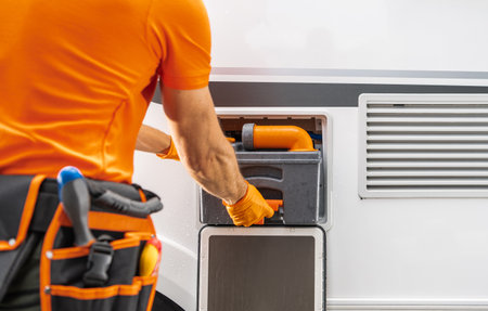 A technician dressed in an orange shirt is engaged in maintenance work on a vehicle's waste disposal system. The scene captures the individual using tools to ensure proper functionality. Bright sunlight enhances the setting.の写真素材