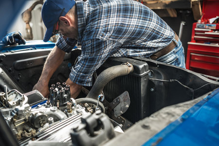 A skilled mechanic is focused on repairing an engine in a well-equipped garage. Tools and car parts are neatly organized around him as he inspects and adjusts components, demonstrating expertise and precision.の写真素材