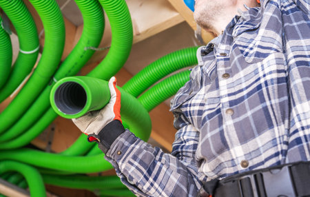 A worker is shown in a workshop, standing underneath a ceiling lined with bright green hoses. He is holding one of the hoses, preparing it for use. The atmosphere is focused and organized, reflecting a practical environment for construction or craft projects. Safety precautions are observed.の写真素材