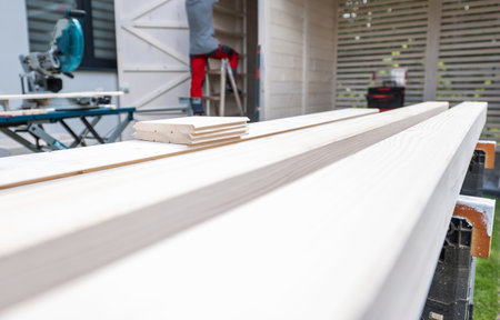 A skilled carpenter is focused on a wood project in a residential yard, with planks laid out on a...