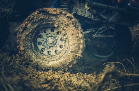 A robust off-road vehicle struggles through muddy ground, its large tires spinning to gain traction....