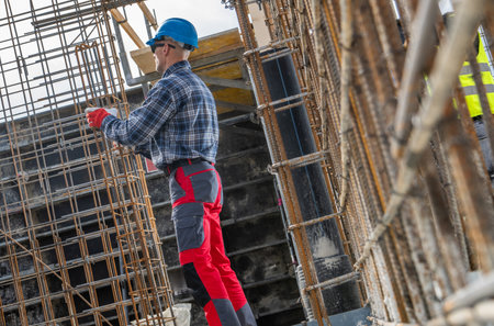 A construction worker, dressed in a blue hard hat and gloves, stands focused on reinforcing steel...